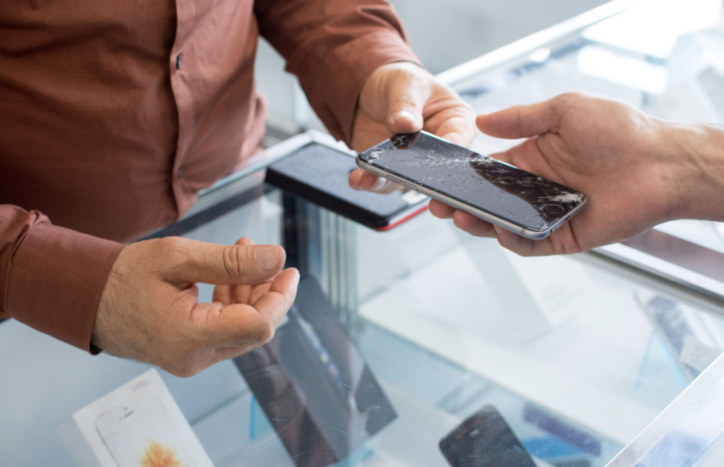 man handling over a cracked smartphone at a store